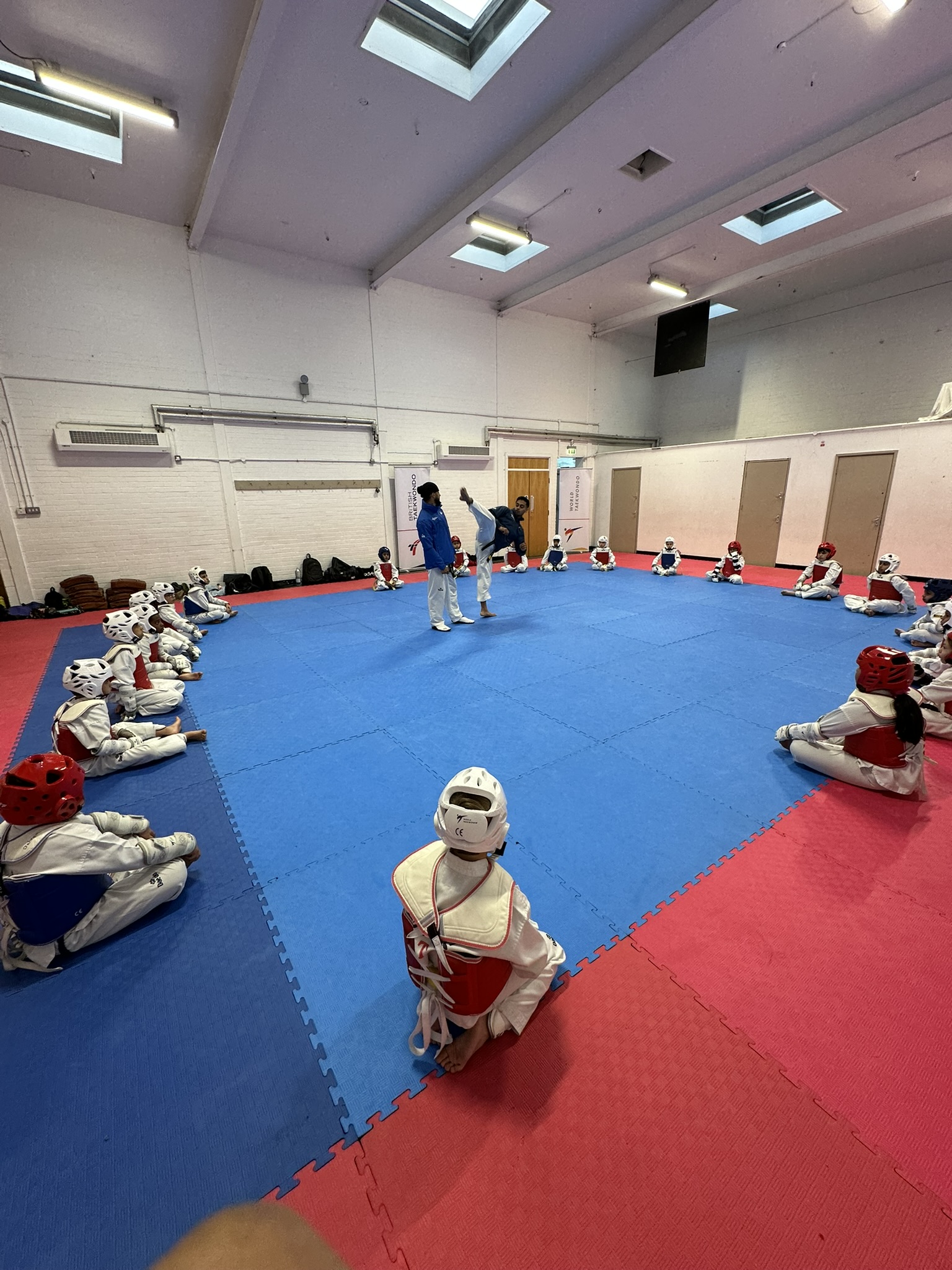 Young students seated in a circle watching a coach demonstrate