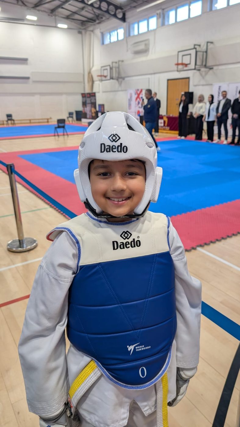 A smiling young fighter in a Daedo head guard and blue chest guard